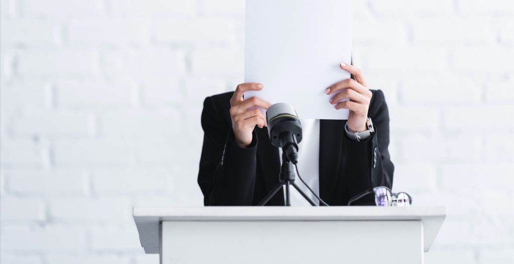 young lecturer, suffering from fear of public speaking, standing on podium tribune and hiding face